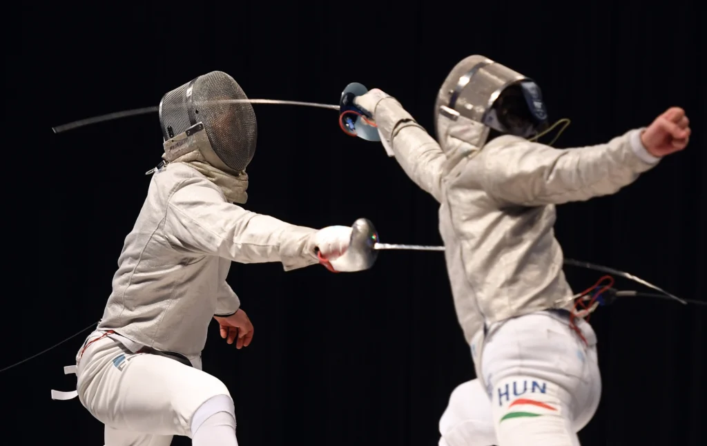 Two sabre fencers in action, engaged in a duel with protective gear and sabres raised.