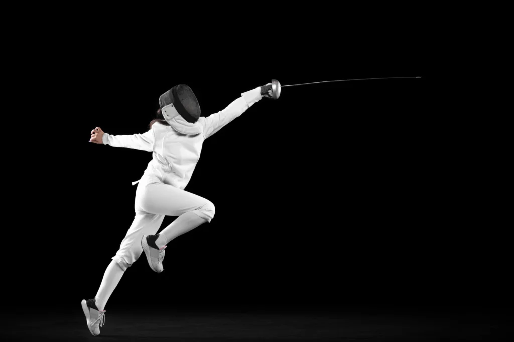 Fencer performing an advanced technique in mid-air, wearing full protective gear against a black background.