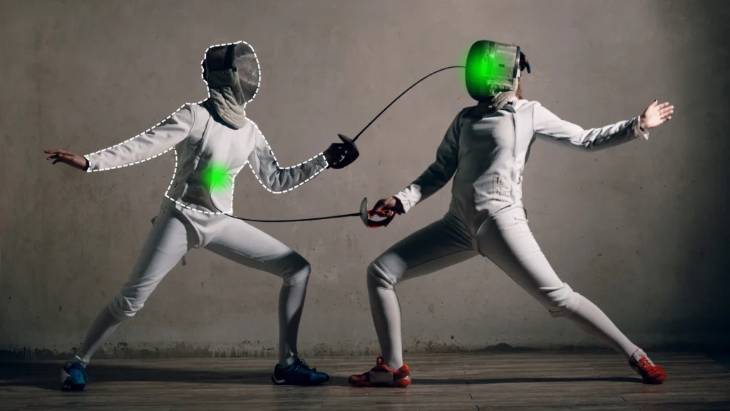 Two fencers in gear face off, with green target areas on their torso and mask.
