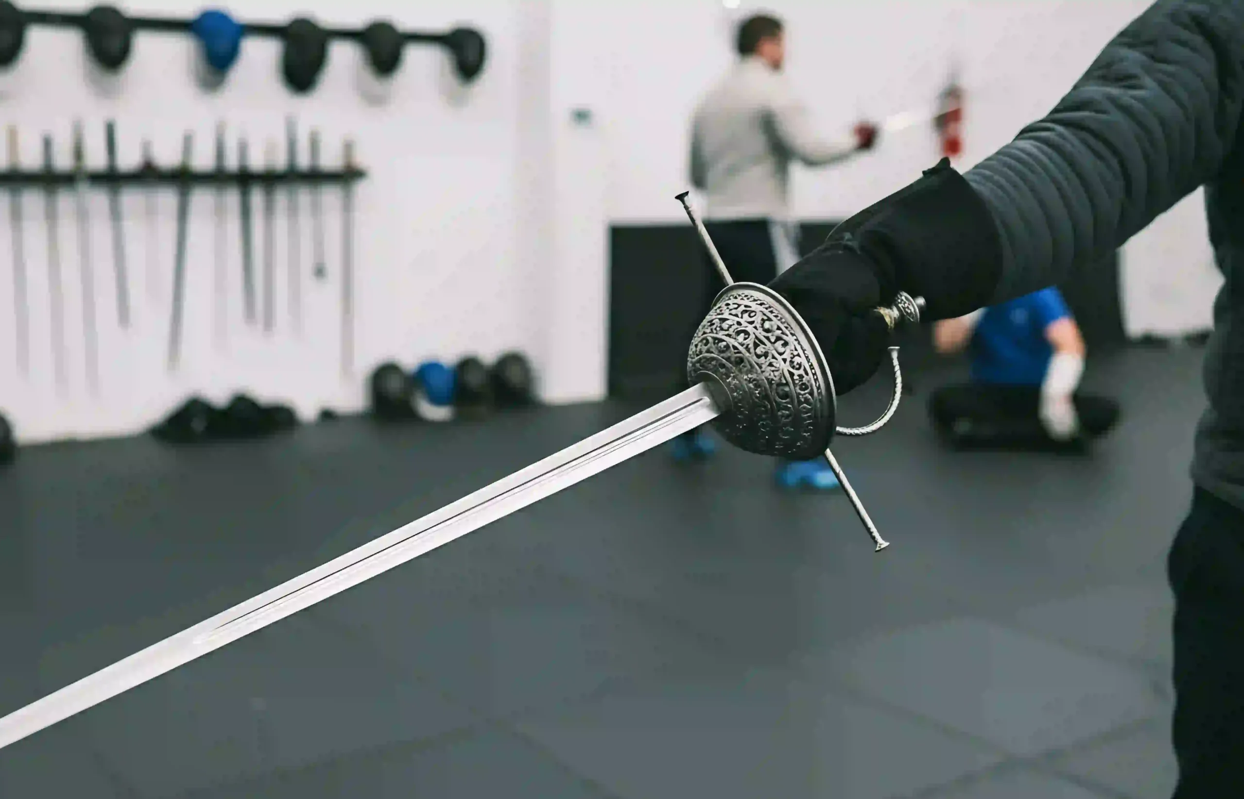 Man holding a real cup guard rapier inside sparing room